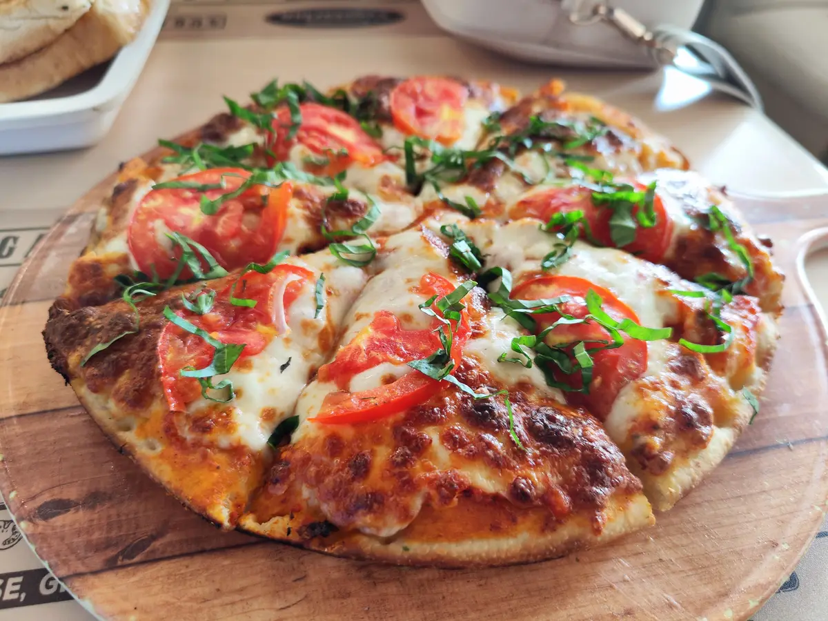Pizza med tomat, smält ost och färsk basilika på ett träfat